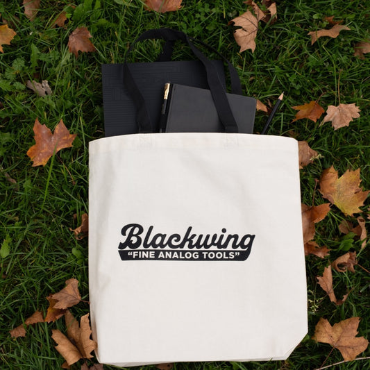 Blackwing Analog Tote Bag filled with analog tools laying on green grass outside