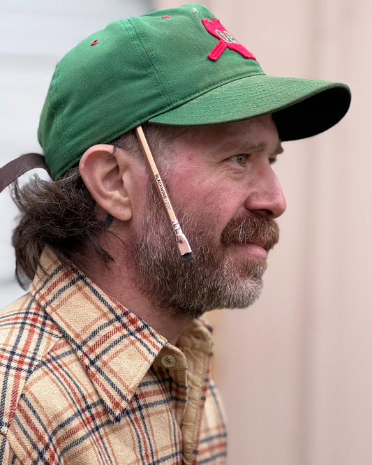 Stephen "Sap" King side profile photo wearing a green baseball cap and a plaid shirt, with a blackwing gold pencil tucked into the side of his cap.