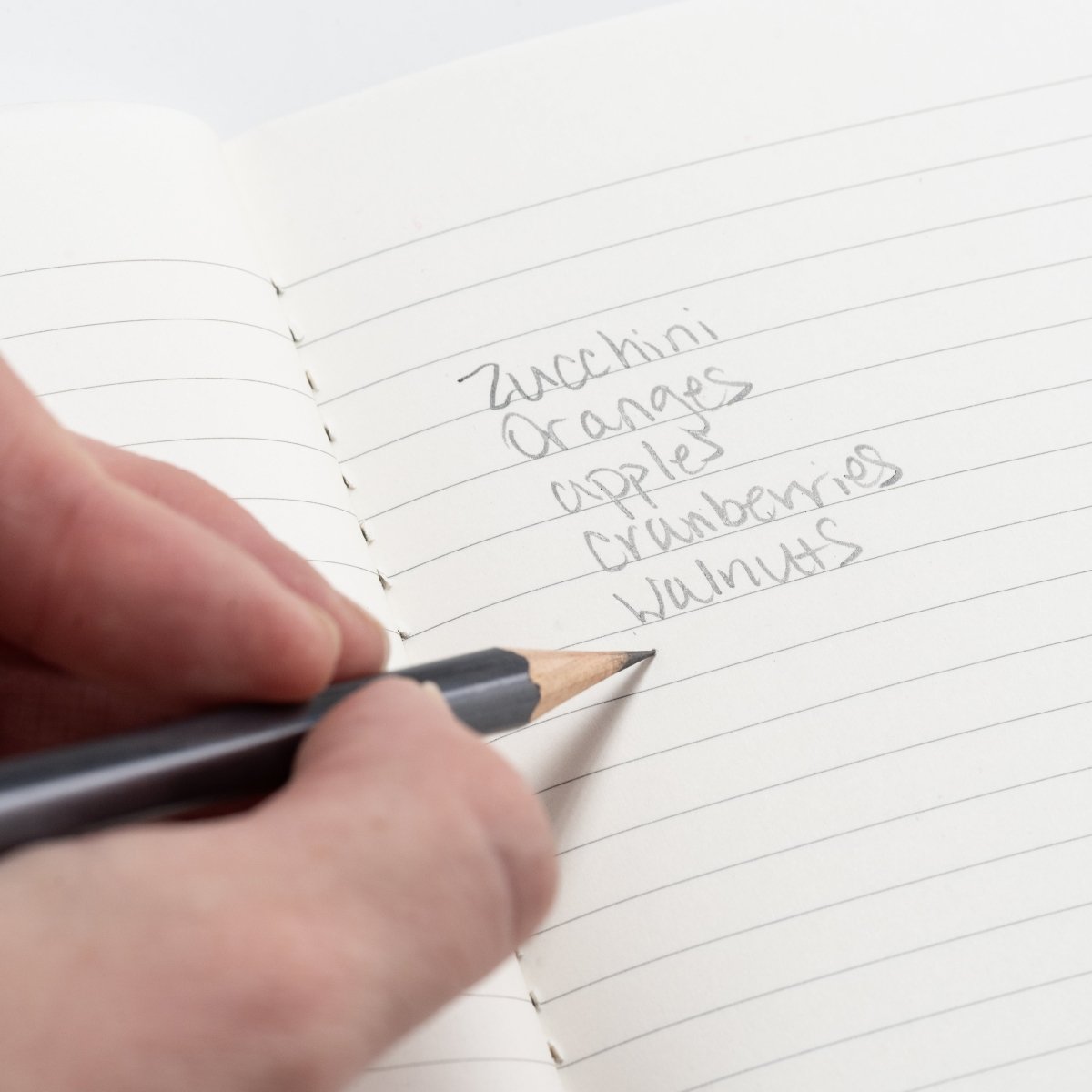 person writing grocery list in memo book