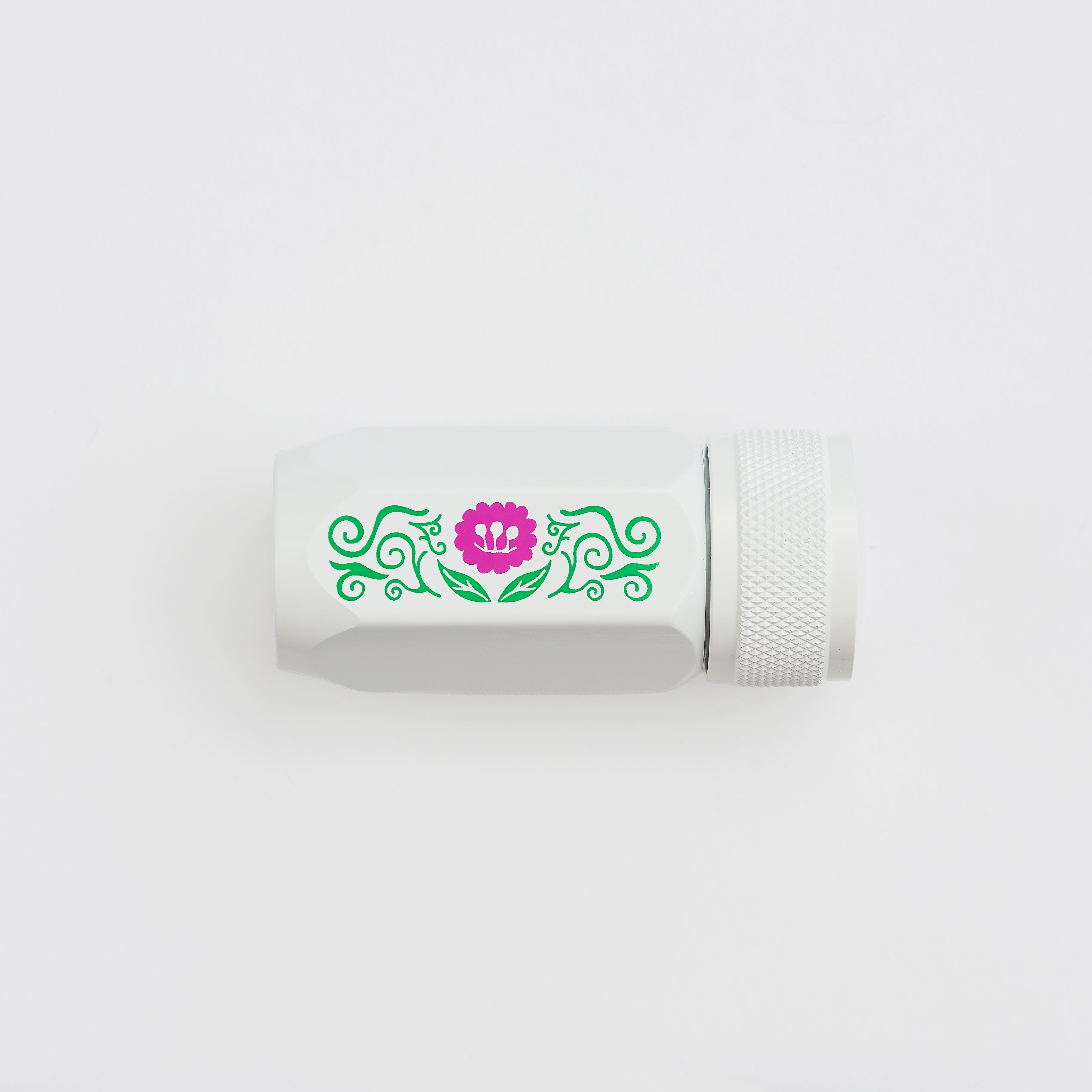 A white cylindrical pencil sharpener with a textured screw-on cap, featuring a decorative green scroll pattern and a pink flower graphic on the side, set against a plain white background.