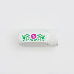 A white cylindrical pencil sharpener with a textured screw-on cap, featuring a decorative green scroll pattern and a pink flower graphic on the side, set against a plain white background.