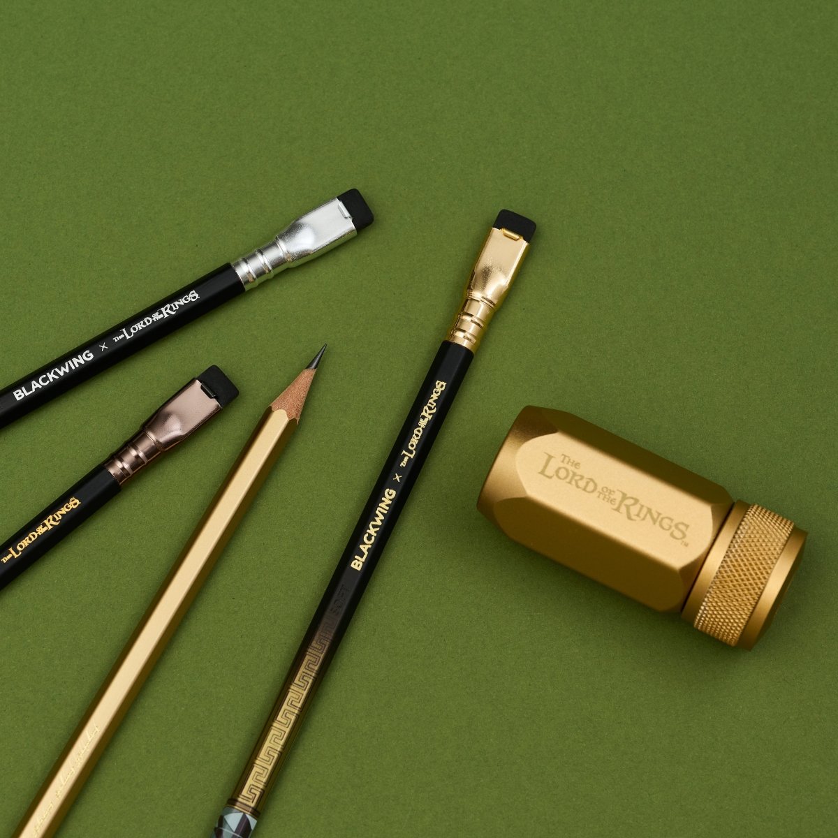 The Lord of the Rings Blackwing pencils next to a gold sharpener on a green background