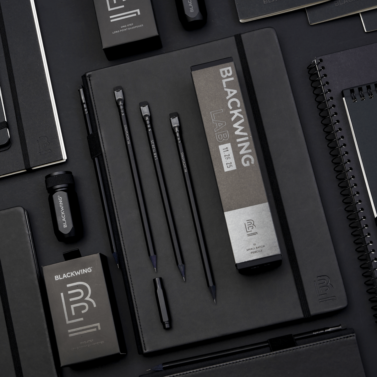 Blackwing products in all black, featuring a black sharpener, black pencils, black point guard, and black notebooks