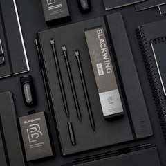 Blackwing products in all black, featuring a black sharpener, black pencils, black point guard, and black notebooks