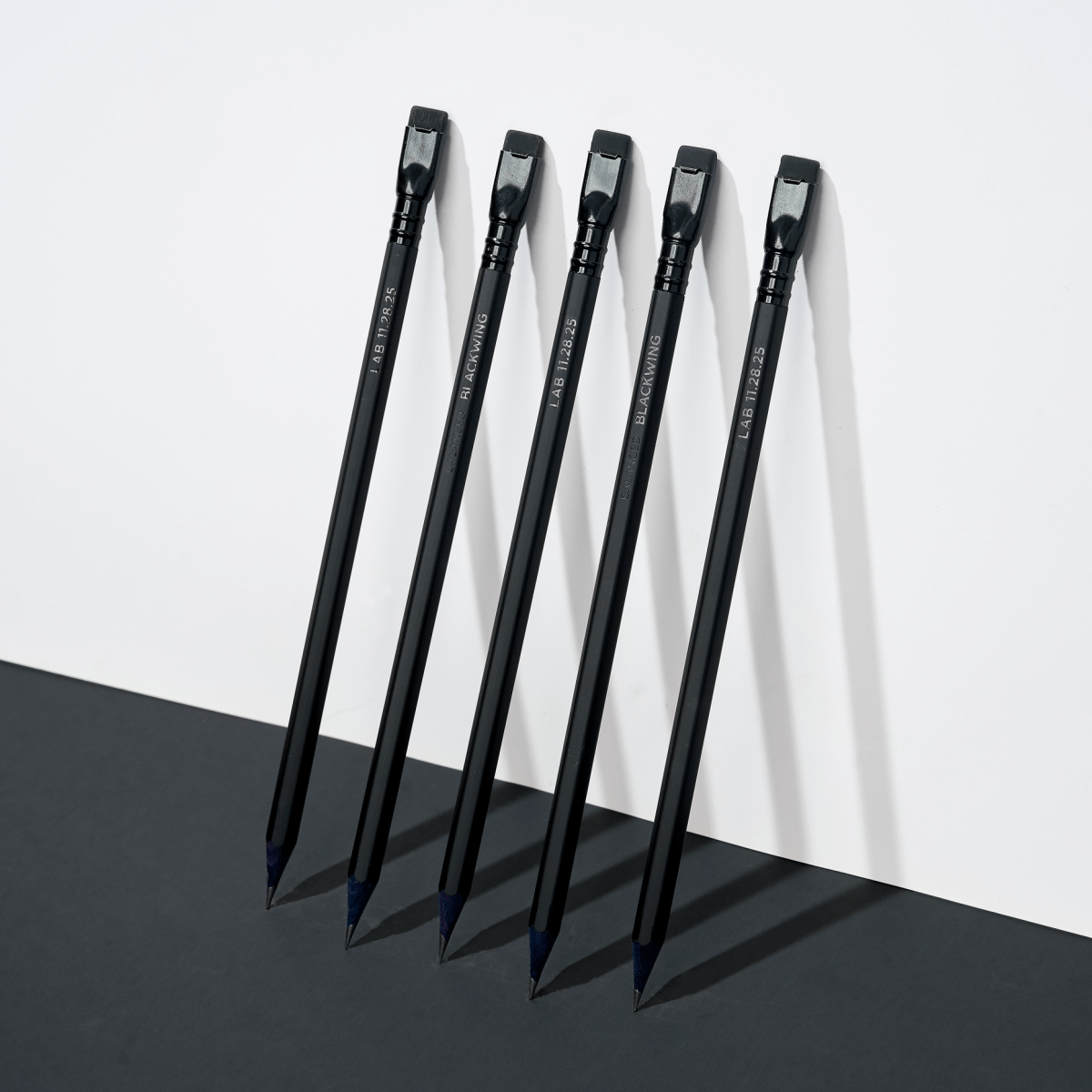 five black pencils leaning against a white wall