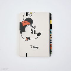 Back of a hardcover notebook featuring a large cartoon Minnie Mouse face, with the Disney logo printed below. The cover is an off-white color and is shown standing upright on a white background, with colorful matching pencil in the pencil holster on the right side.