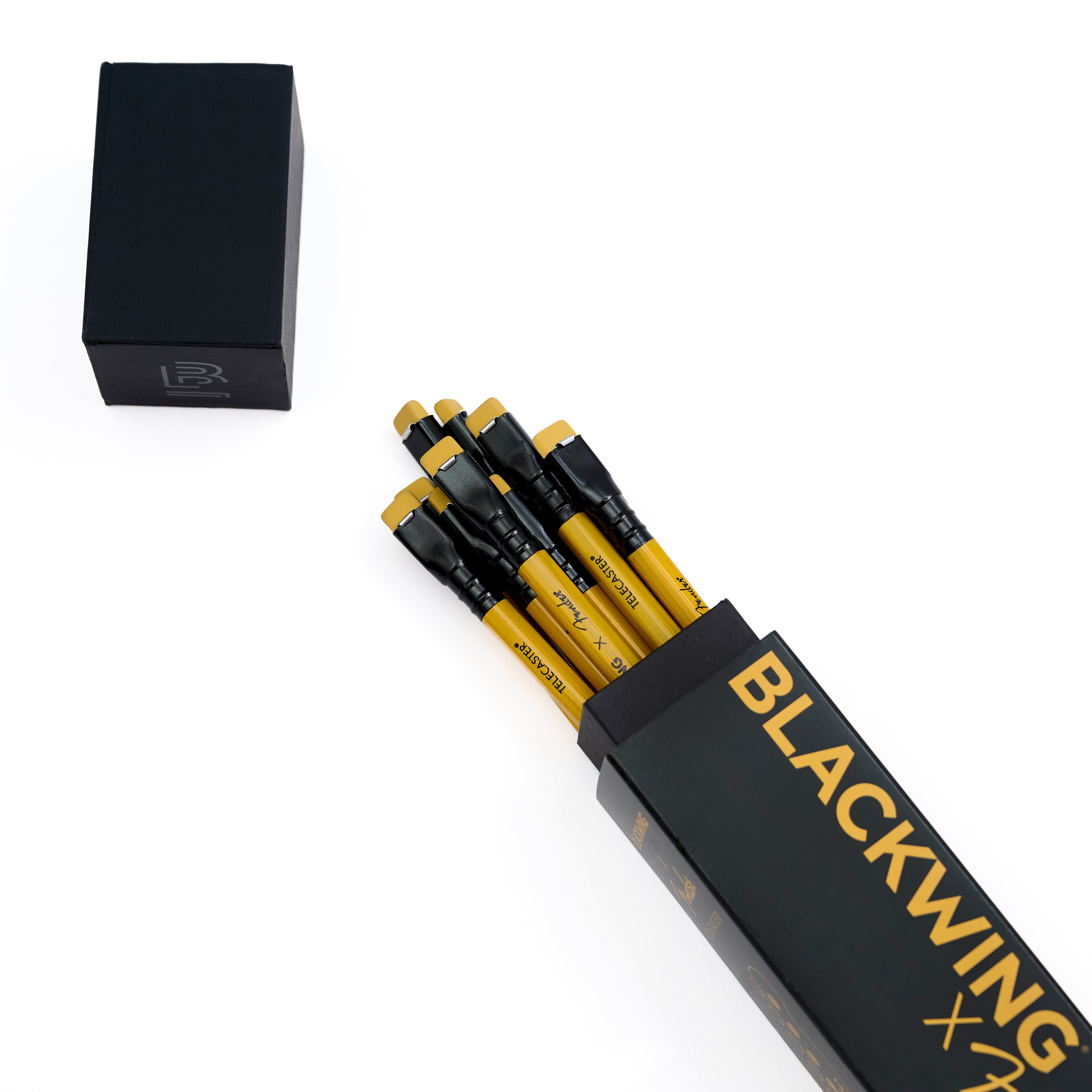 A set of black and yellow pencils partially pulled from a black rectangular box with gold 'BLACKWING' lettering, shown on a clean white background with a separate black lid at the upper left.