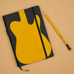 A Blackwing hardcover notebook in black with a large yellow guitar-shaped graphic on the cover to honor the Fender Telecaster Butterscotch, placed on a tan background next to a matching yellow and black pencil.