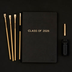 Black notebook with 'Class of 2026' gold foil stamped imprint with 4 gold pencils, a black sharpener, and a gold point guard on a black background