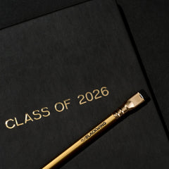 'Class of 2026' black notebook and a gold pencil on a black background