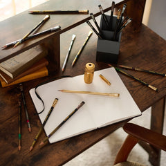 Blackwing x Lord of the Rings pencils scattered on a wood desk with a notebook, sharpener, and point guard