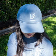 person sitting on the grass wearing a blue baseball cap with 'B' emblem stitched on the front and a matching blue t-shirt 