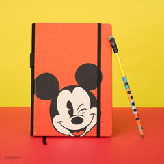 A red Disney Mickey Mouse notebook done with Blackwing that features a black elastic closure, standing next to a colorblock Mickey-themed pencil on a red and yellow background.