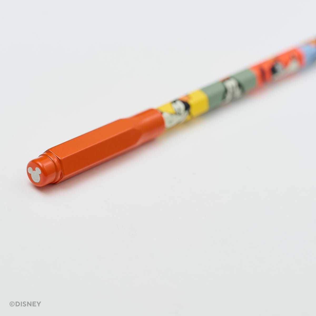 A close-up of a Disney pencil with a bright red cap and a multicolor body featuring cartoon character illustrations, photographed on a clean white background.