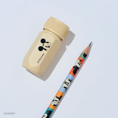 A Disney pencil and pencil sharpener set on a light gray background. The sharpener is a light beige aluminum hexagonal tool with a black Mickey Mouse graphic and the Disney name. The pencil barrel features various Mickey Mouse face graphics in different colorblocks.