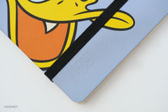 A close-up of a light blue Disney Blackwing notebook with a black elastic closure band and a cartoon Donald Duck face printed on the cover. A Disney watermark is visible in the bottom-left corner.