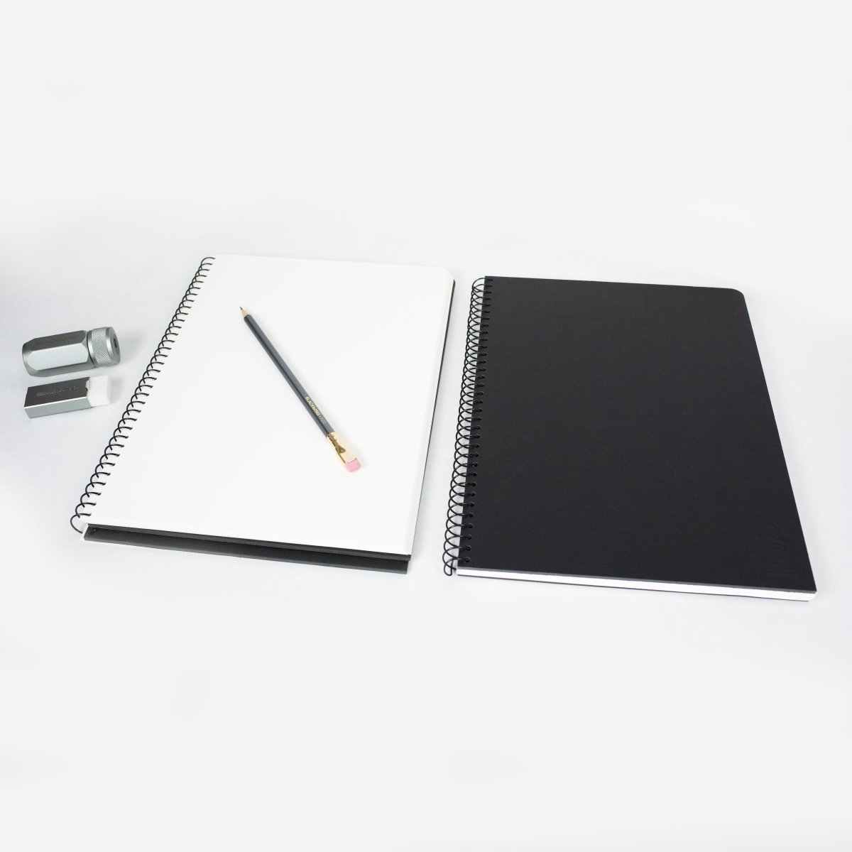 2 Blackwing Spiral Notebooks, a 602 pencil, a handheld eraser, and a one-step sharpener on a white background.