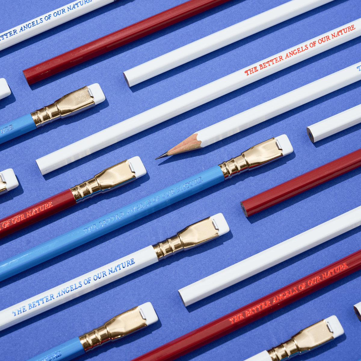 pencils that say 'THE BETTER ANGELS OF OUR NATURE' in red, white, and blue colorways arranged on a blue background