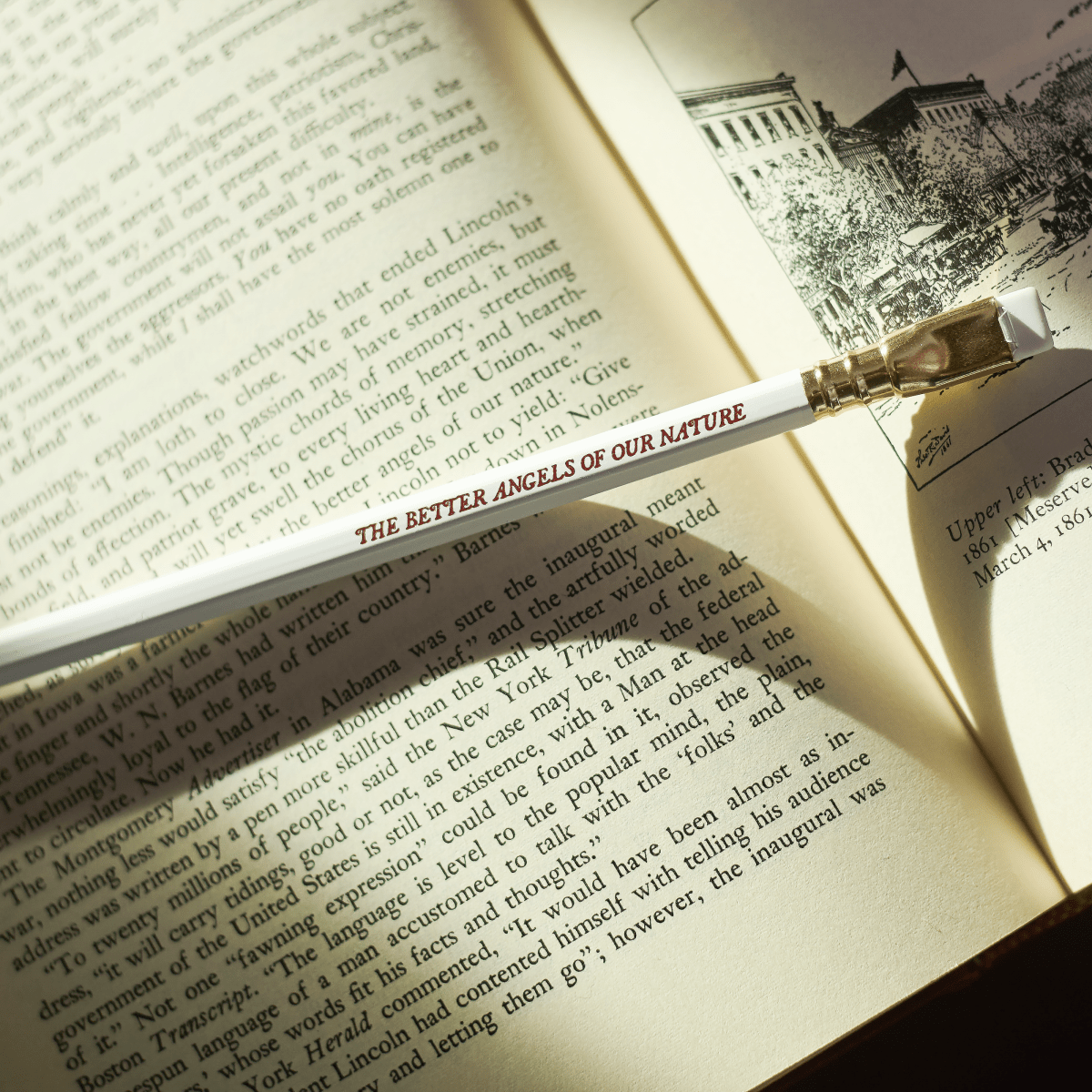 white pencil with red imprint that says 'THE BETTER ANGELS OF OUR NATURE' on top of an open book
