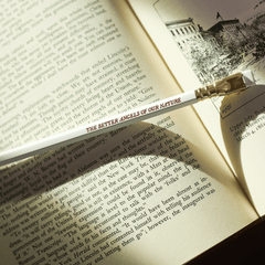 white pencil with red imprint that says 'THE BETTER ANGELS OF OUR NATURE' on top of an open book