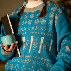 person wearing a blue and grey pencil sweater and holding a notebook and coffee mug