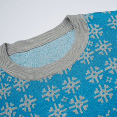 Close-up of a blue sweater with a geometric snowflake pattern and gray neckline.