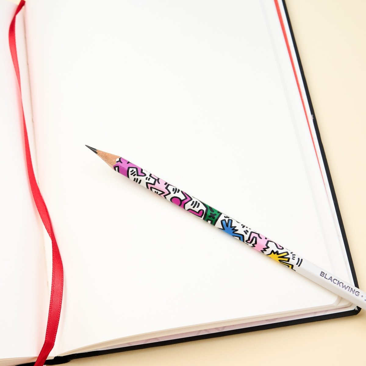 Blackwing Volume 292 Keith Haring Notebook open on a table with a Keith Haring "Dancing Figures" pencil