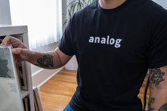 person wearing a black cotton t-shirt with the word analog in white across the chest