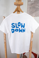 back of white slow-down t-shirt with blue screen printed "slow down" text across upper back